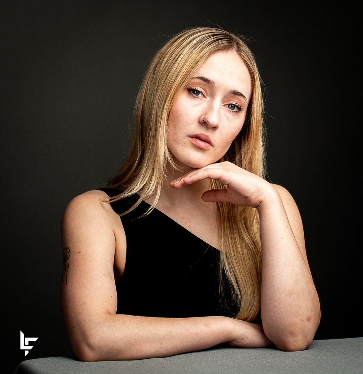 Studio portrait of a blonde woman in black, resting her chin on her hand.